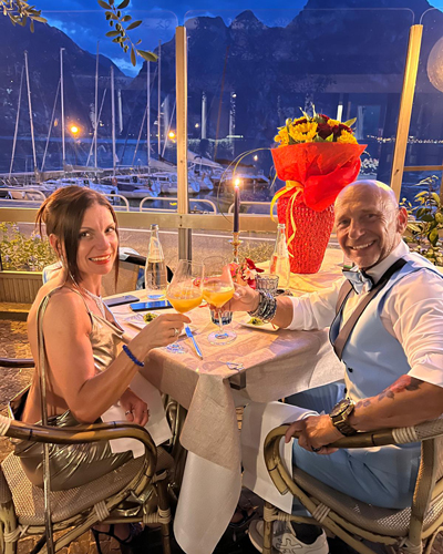 Couple toasting drinks at a romantic outdoor restaurant with mountain and marina views. Fine dining.