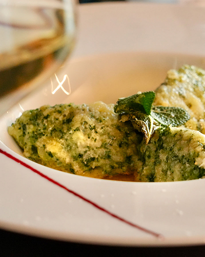 Delicious ricotta and spinach gnocchi with sage butter sauce on a white plate, paired with a glass of white wine.