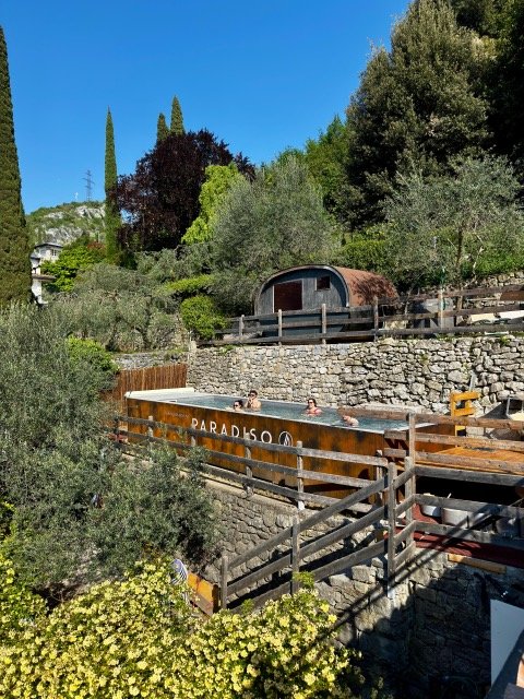 Paradiso outdoor pool with people relaxing, surrounded by lush greenery and stone walls, creating a serene vacation vibe.